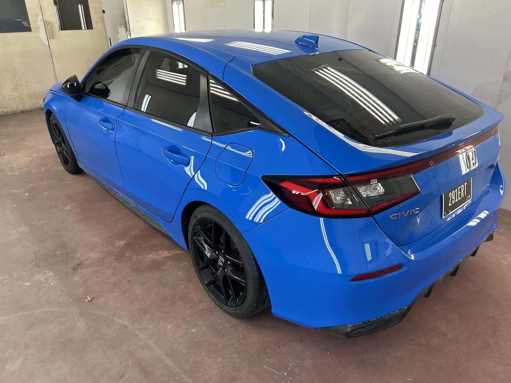 Blue Honda Civic sedan parked indoors, showing the rear and side view with black wheels, tinted windows, and a sunroof.
