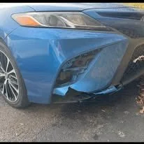 Blue car with front-end damage, including a bent bumper and misaligned headlight.