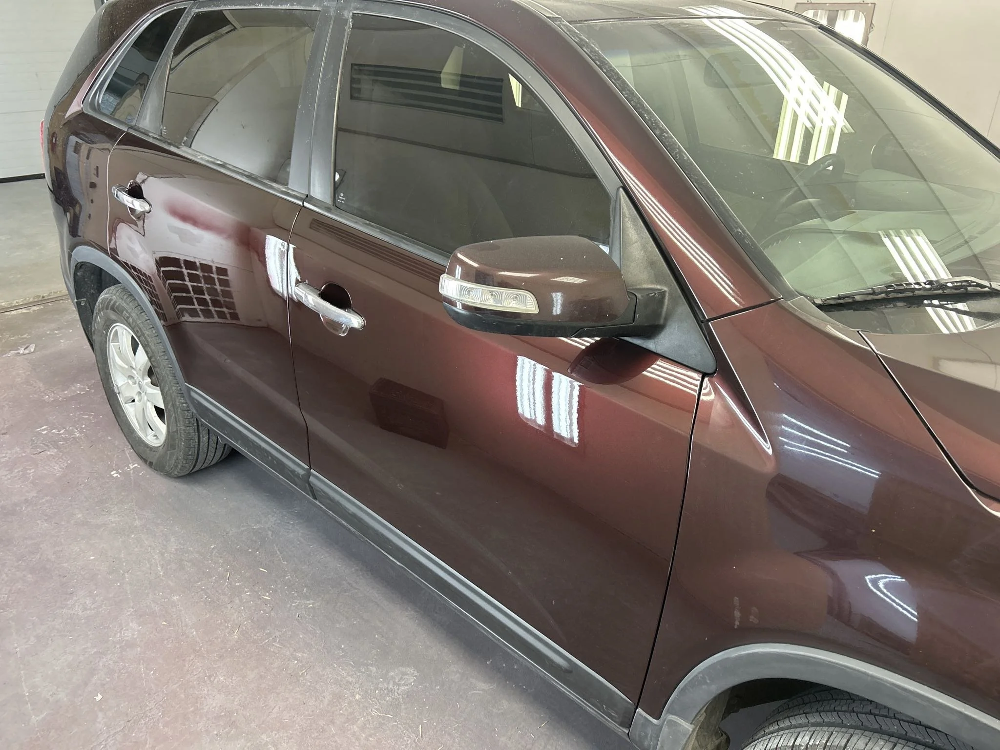 A dark red SUV parked indoors, with reflections of ceiling lights on its surface.