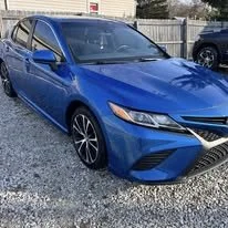 A blue sedan parked on a gravel lot with a fence and trees in the background.