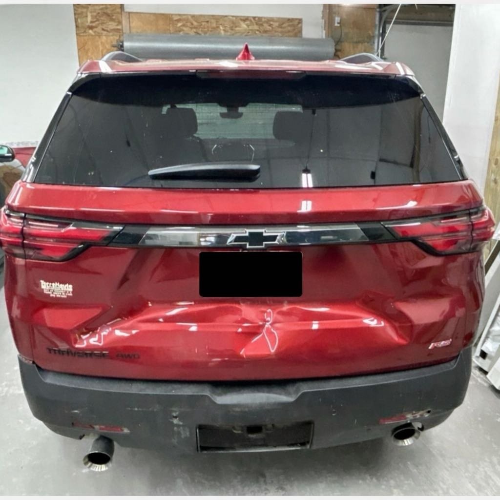 Red Chevrolet SUV with rear damage, parked in a garage, with a black license plate, dual exhaust pipes, and a Chevrolet emblem on the back.