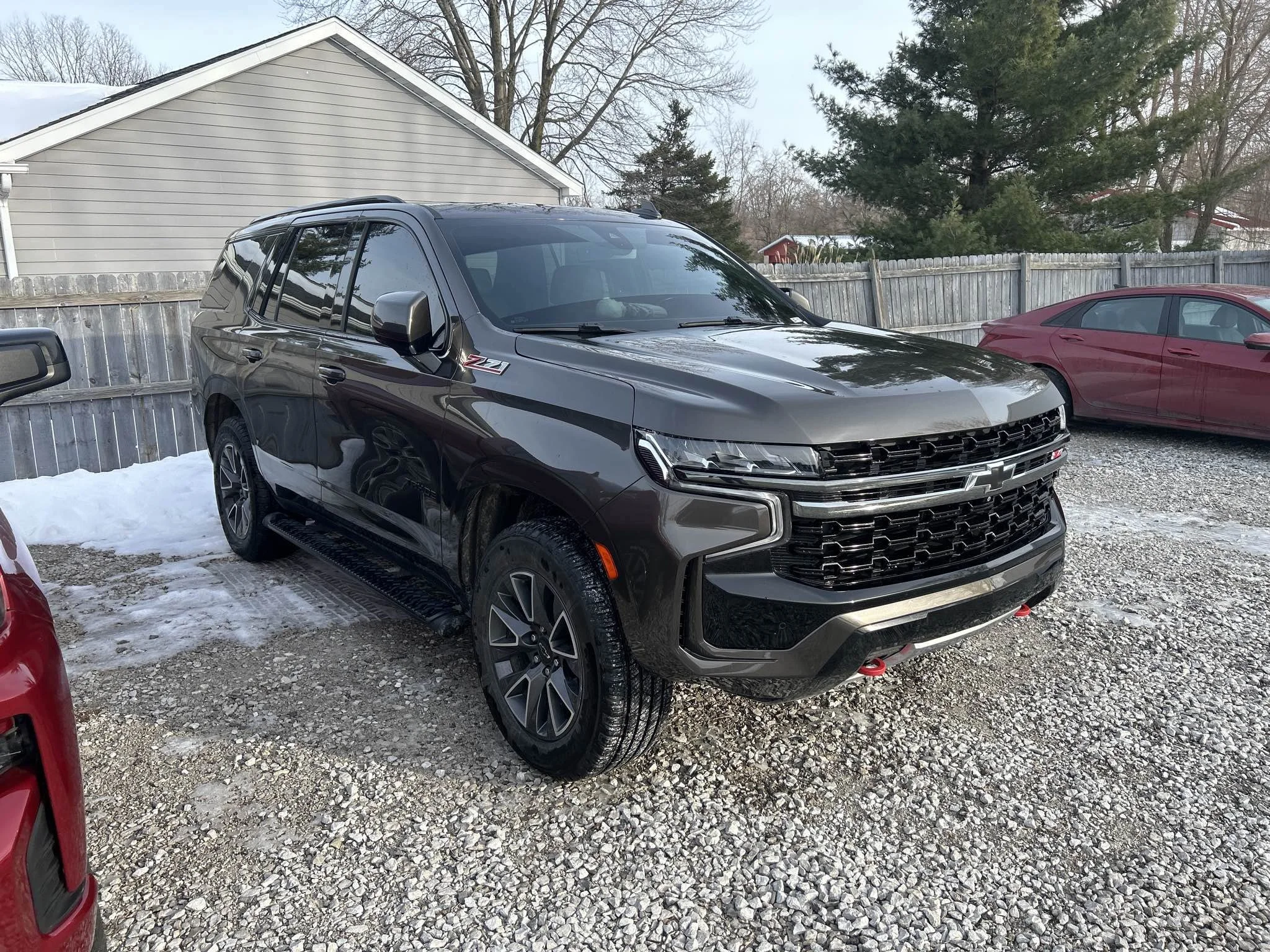 Black Chevrolet SUV parked on a gravel lot in a residential area, with snow on the ground and other cars nearby.