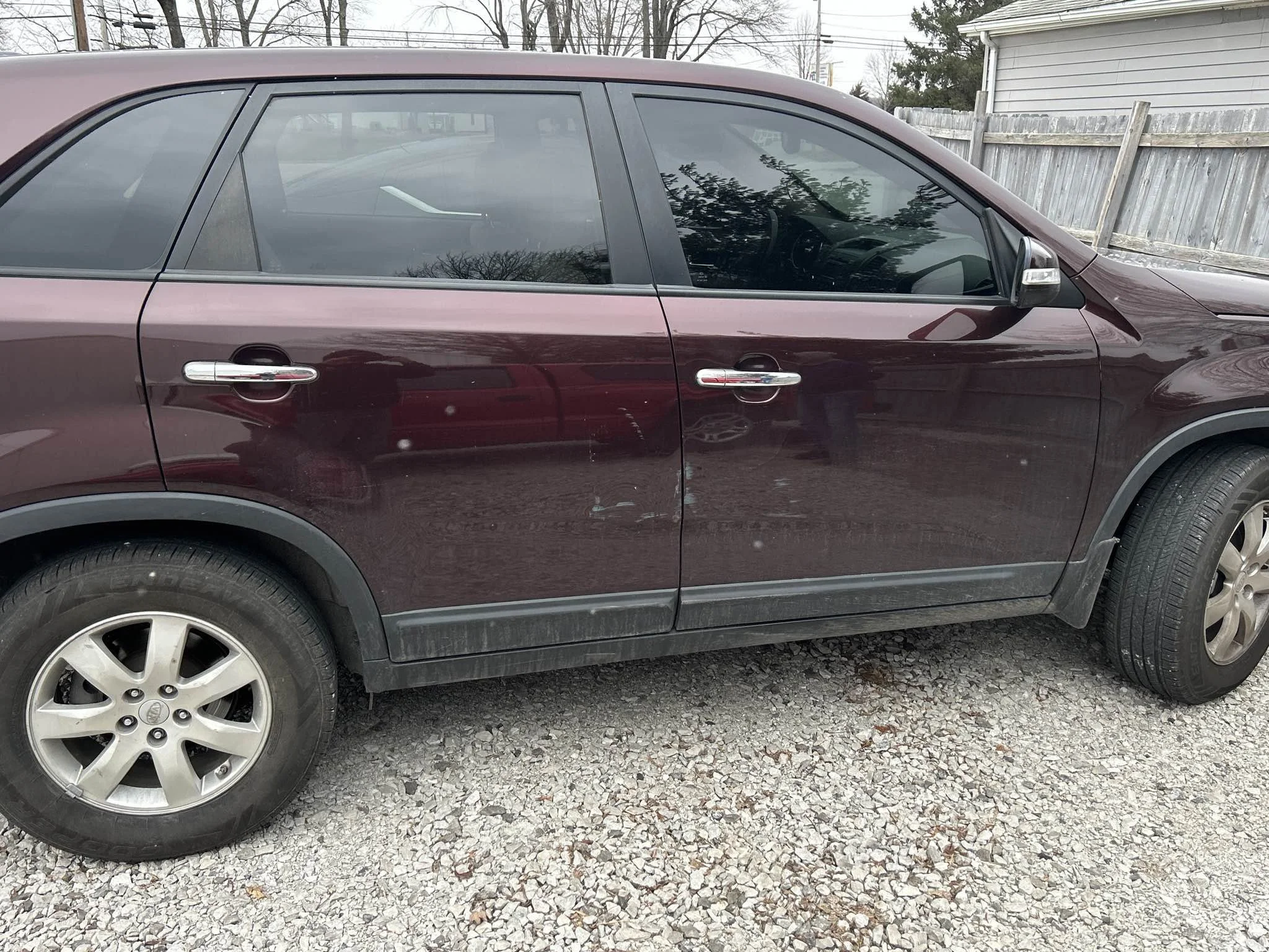 Maroon SUV parked on gravel driveway beside wooden fence and house.