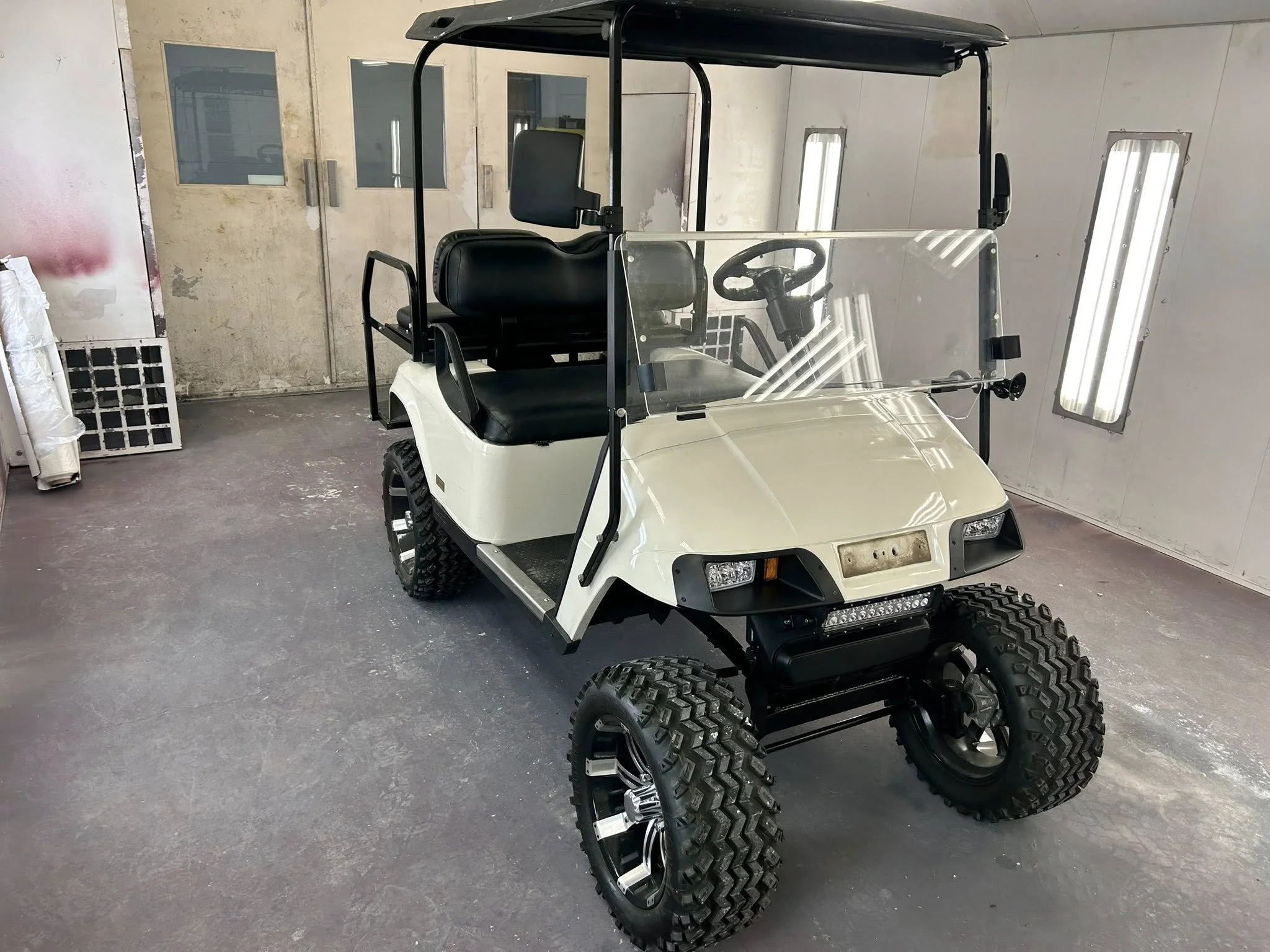 A white golf cart with large off-road tires parked inside an industrial workshop.