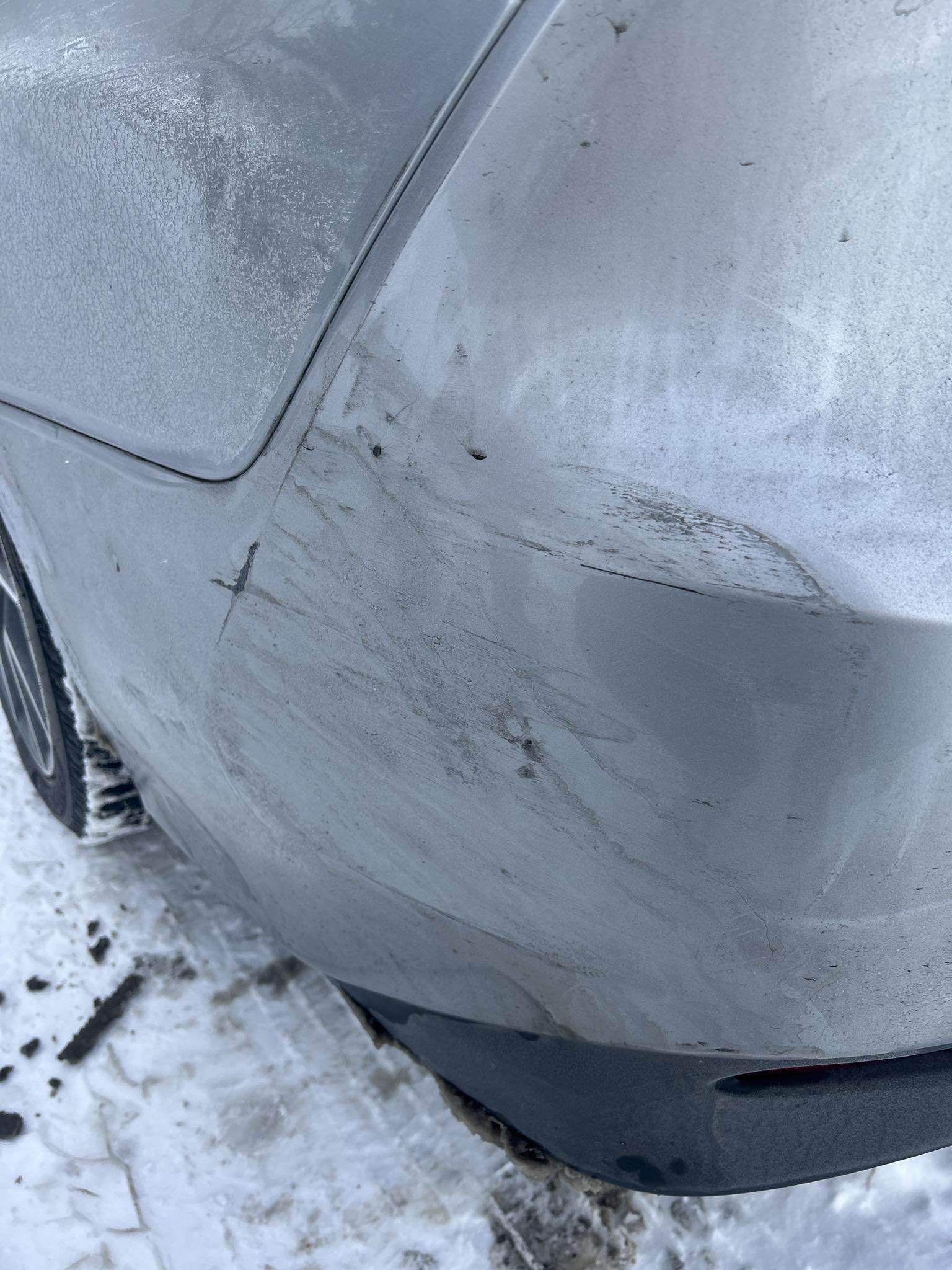 Car with visible damage or scratches on the rear side panel, parked on snow-covered ground.