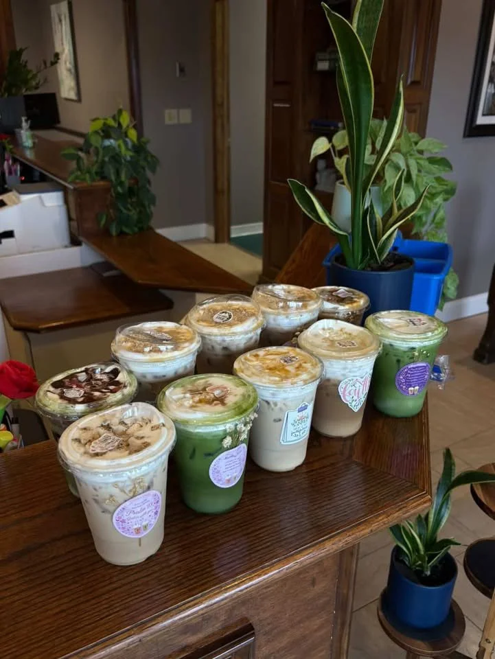 A wooden table with multiple cups of bubble tea or smoothies, topped with toppings, inside a cozy home environment with potted plants.