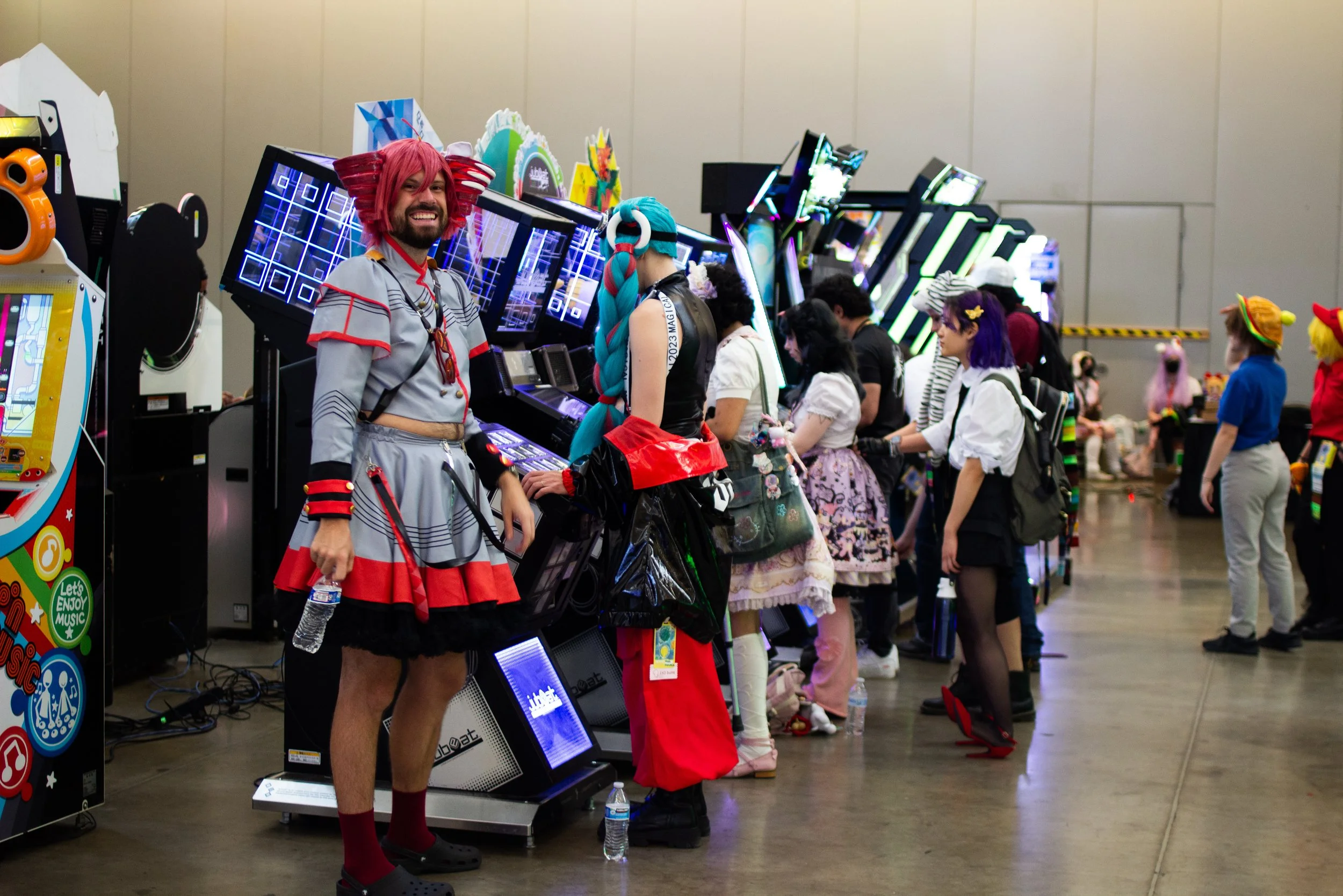 People in colorful costumes at an arcade or gaming event with electronic dance game machines and decorations.