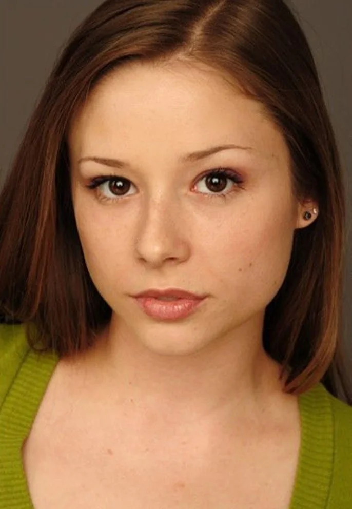 Close-up portrait of a young woman with shoulder-length brown hair, brown eyes, and light skin, wearing a green top and small earrings.