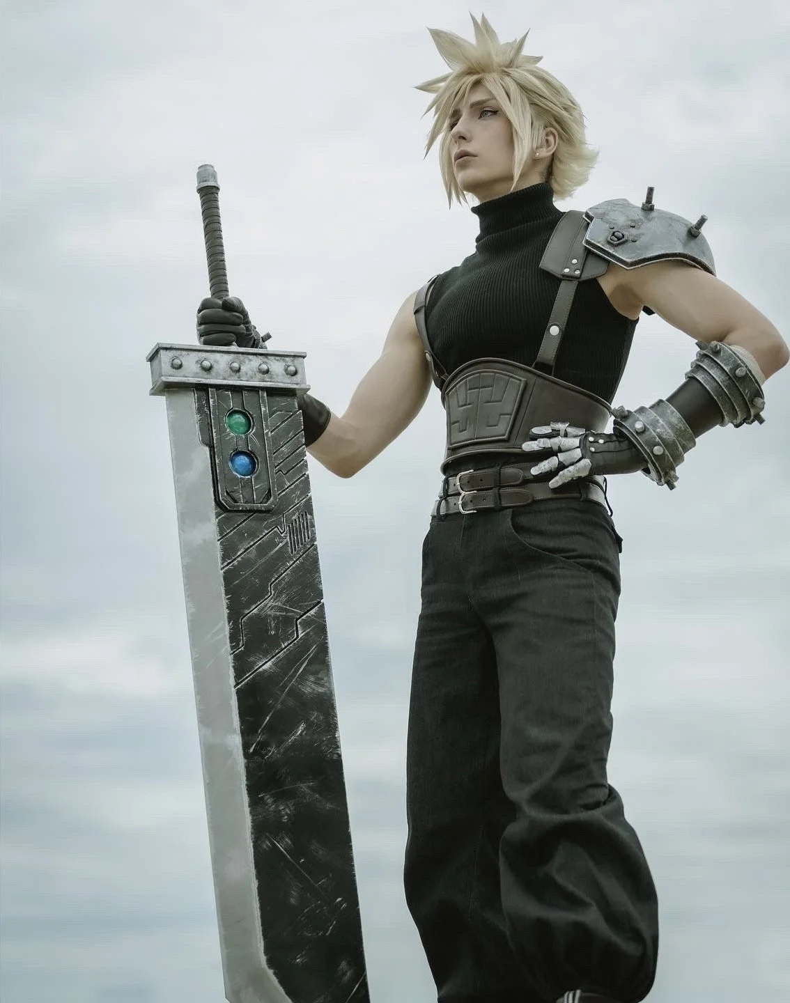 A person dressed as Cloud Strife from Final Fantasy holding a large, stylized sword, wearing black clothing and armor, with spiky blond hair and a cloudy sky in the background.