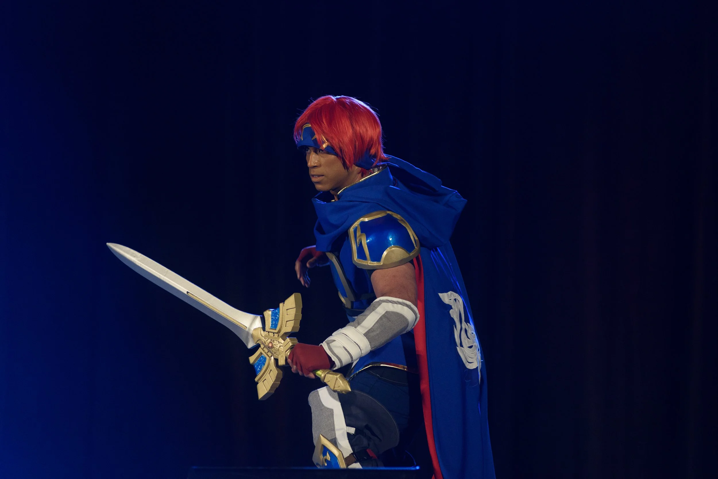 A cosplayer from Fire Emblem brandishes a sword on stage.