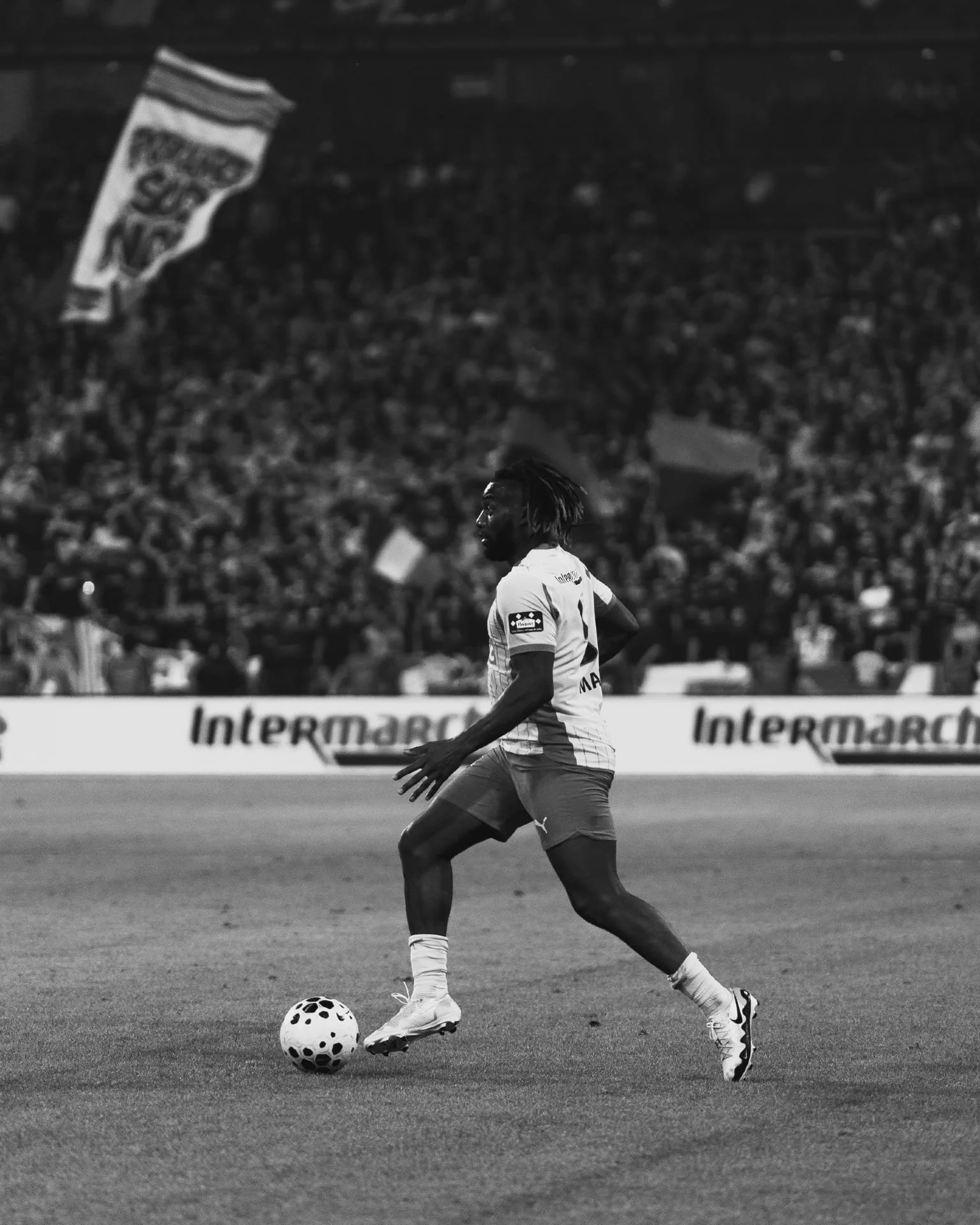 Un joueur de football en action sur le terrain lors d'un match, avec une foule de spectateurs en arrière-plan.