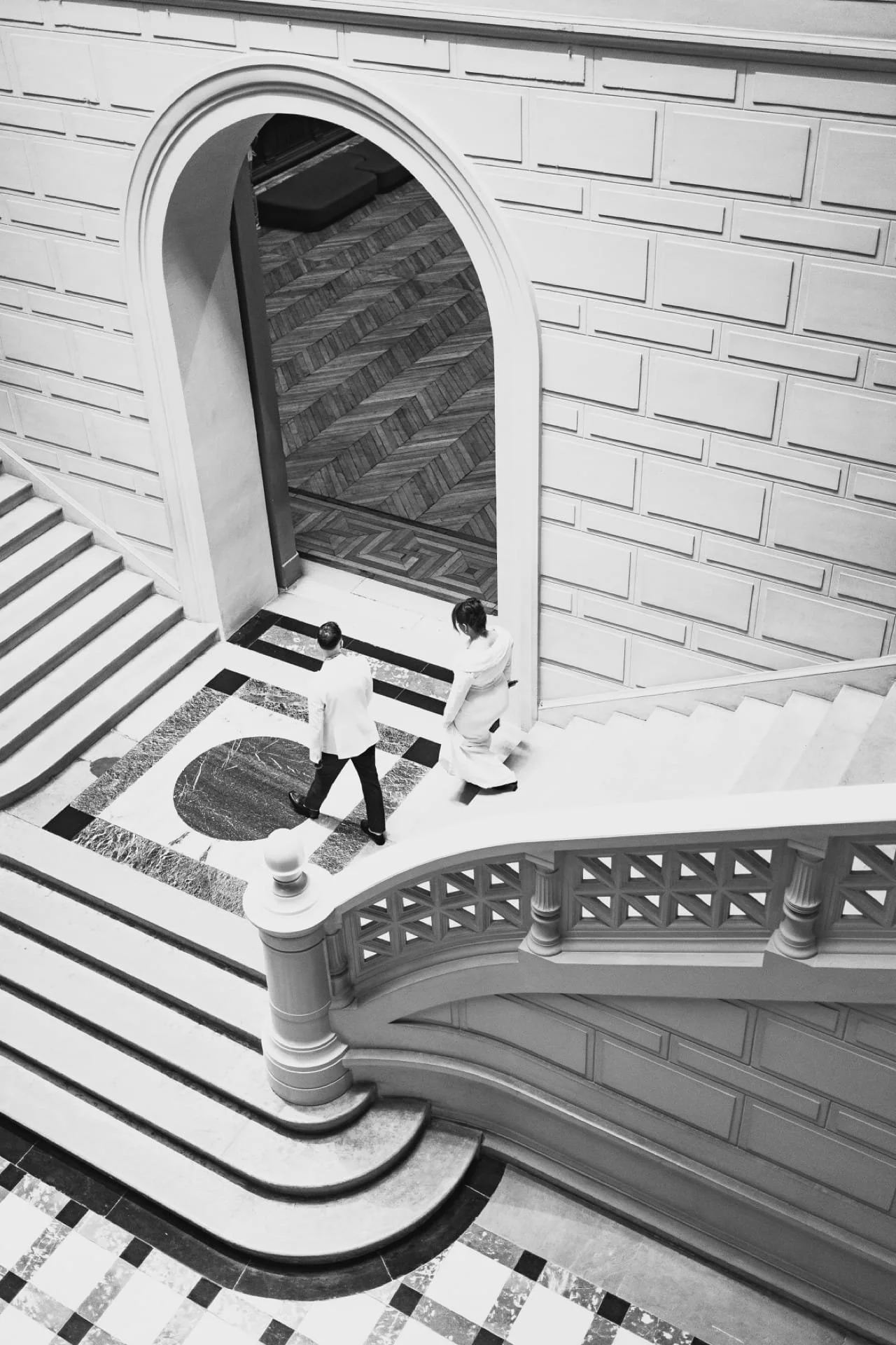 Une vue en noir et blanc d'un intérieur d'immeuble avec un escalier en spirale et des personnes en vêtements professionnels discutant au sol. Cauê Foto, photographe Amiens, photographe de mariage et événementiel