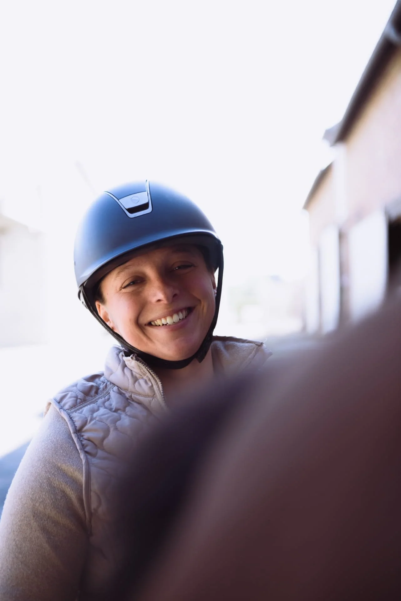 Une femme souriante sur son cheval, portant une bombe à cheval et une veste beige, prise en selfie à l'extérieur par temps ensoleillé. Cauê Foto, photographe Amiens, photographe de mariage et événementiel