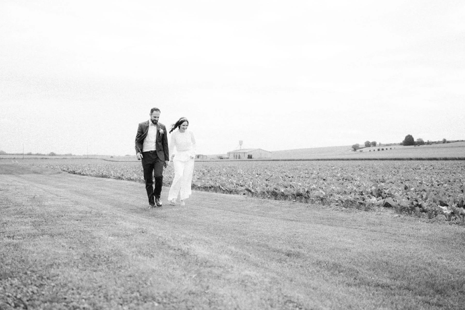 Un couple habillé élégamment marche dans un champ lors d'une journée ensoleillée.