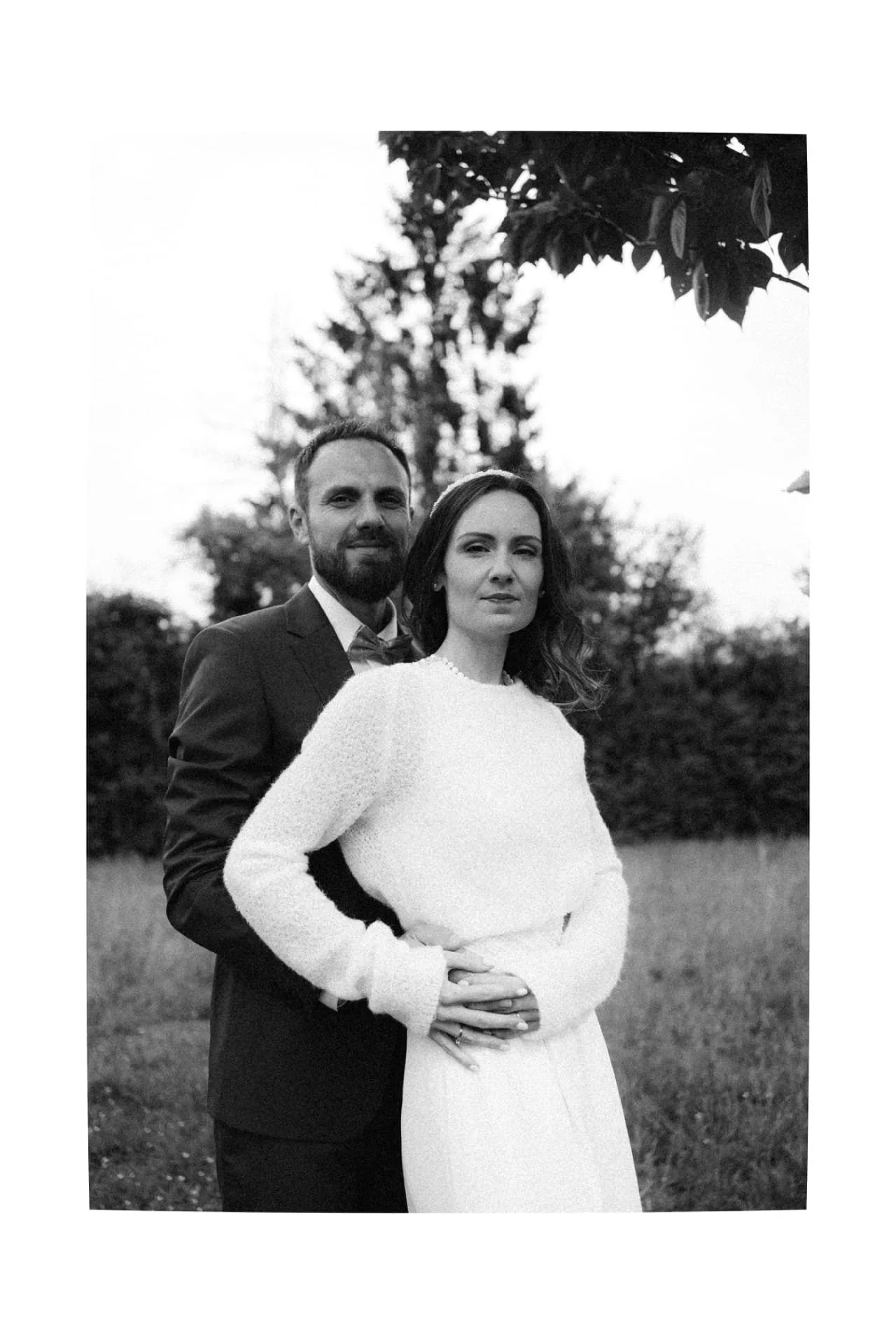 Un couple en tenue habillée, le homme en costume et la femme en robe longue, se tenant dans un champ en extérieur, probablement pour une séance photo ou un événement spécial.