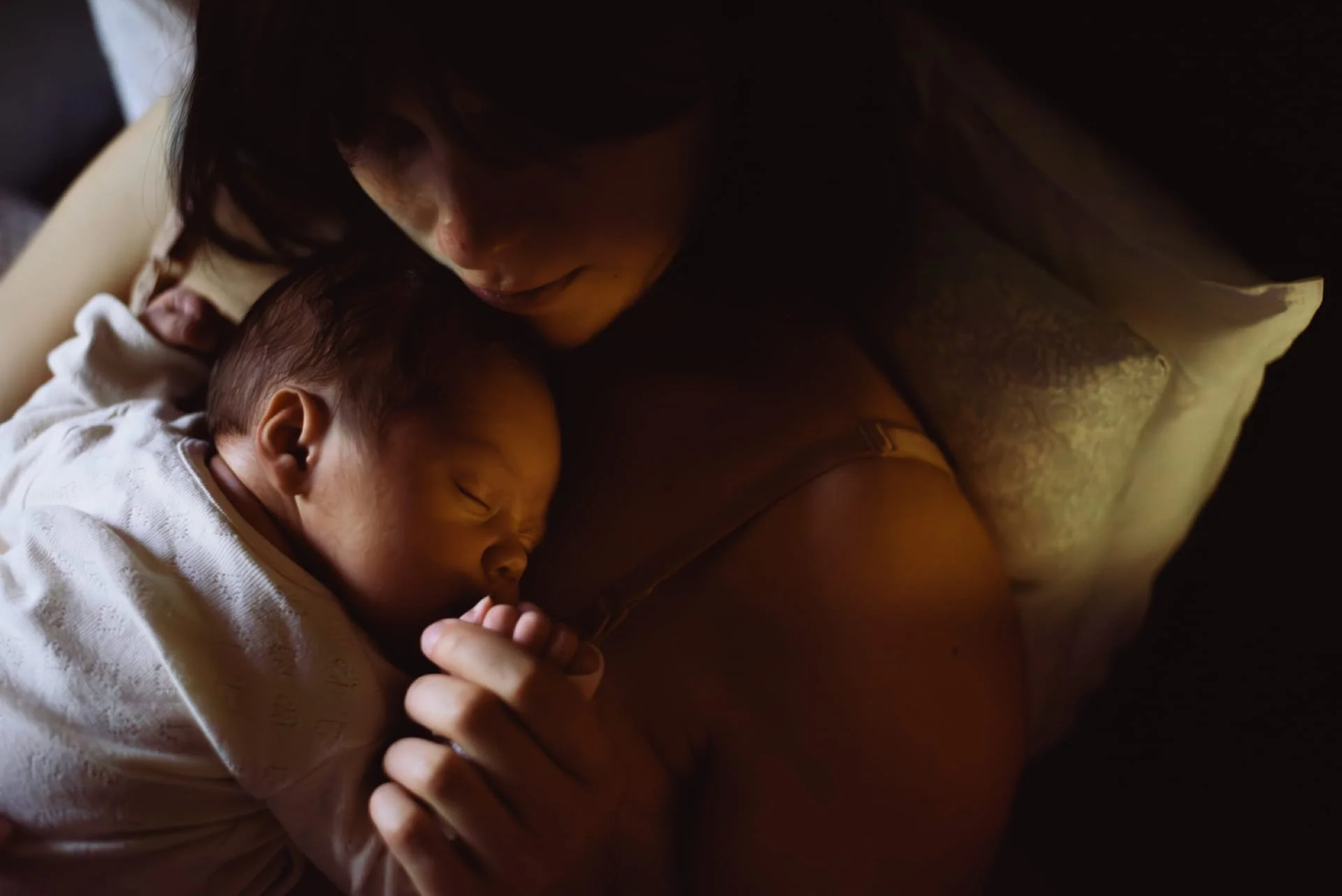 Un bébé endormi qui est tenu par une adulte dans une pièce sombre.