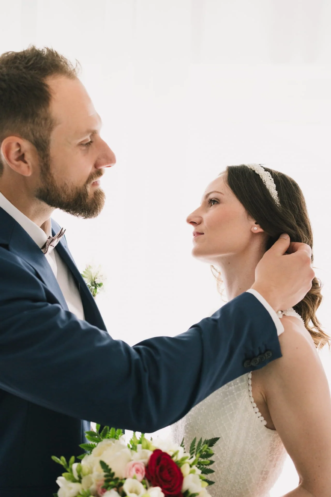 Un couple de mariés lors de leur mariage, l'homme tenant le visage de la femme dans ses mains, avec un bouquet de fleurs en premier plan.