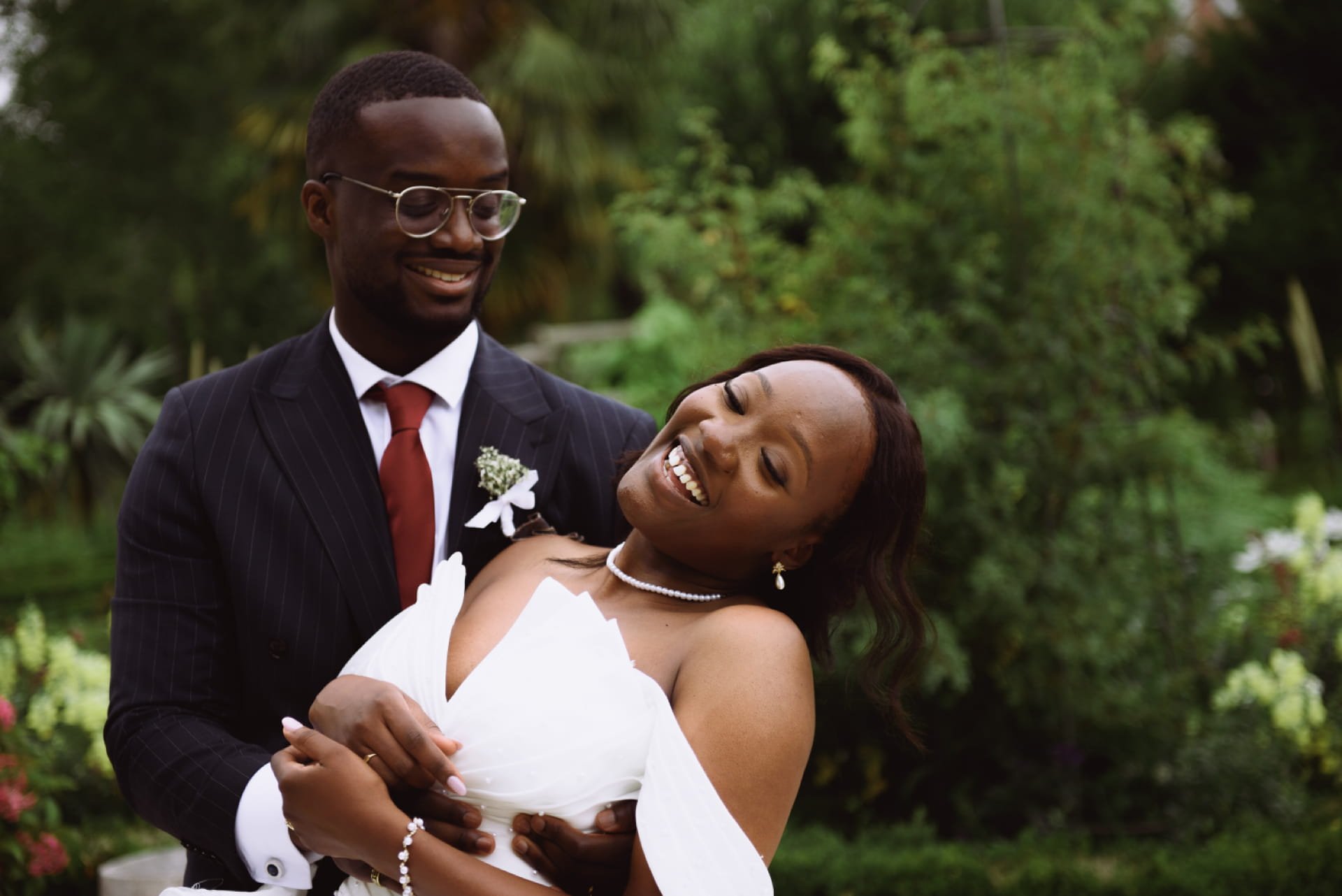 Un couple de mariage, un homme en costume sombre et une femme en robe blanche, danse en extérieur avec un décor verdoyant