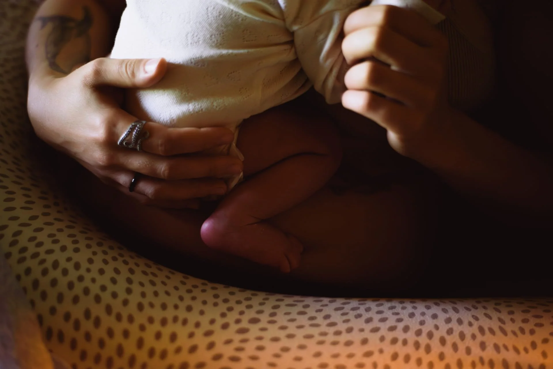 Mains tenant un tissu beige, près d'un bébé couché sur un lit avec une couverture à pois marron, en position fœtale. Cauê Foto, photographe Amiens, photographe de mariage et événementiel