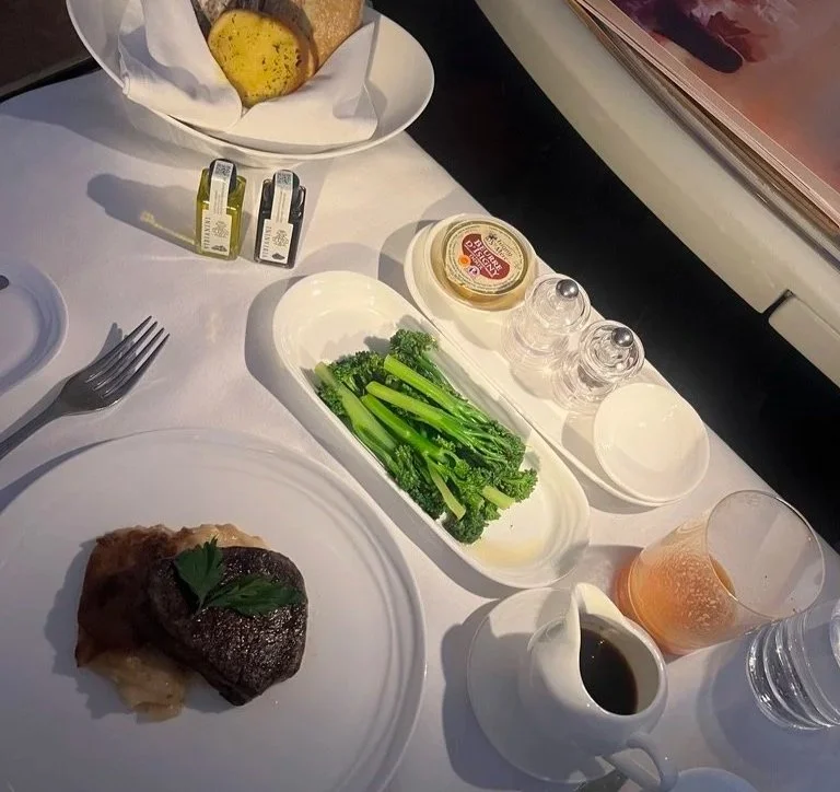 Emirates first-class dining with steak, brocolini, sauce, bread basket and condiments.