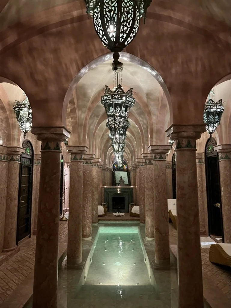 Moroccan spa at La Sultana hotel Marrakech with pink marble columns around a pool of water and Moroccan lights above.