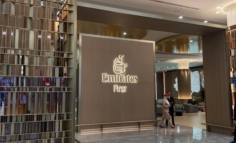 Dubai International Airport Emirates first-class check-in lounge entry with illuminated signage to the right of decorative wall.