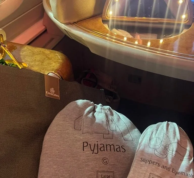 Emirates first-class grey pyjama set, grey slippers and grey fabric tote bag with small illuminated mirror on desk behind.