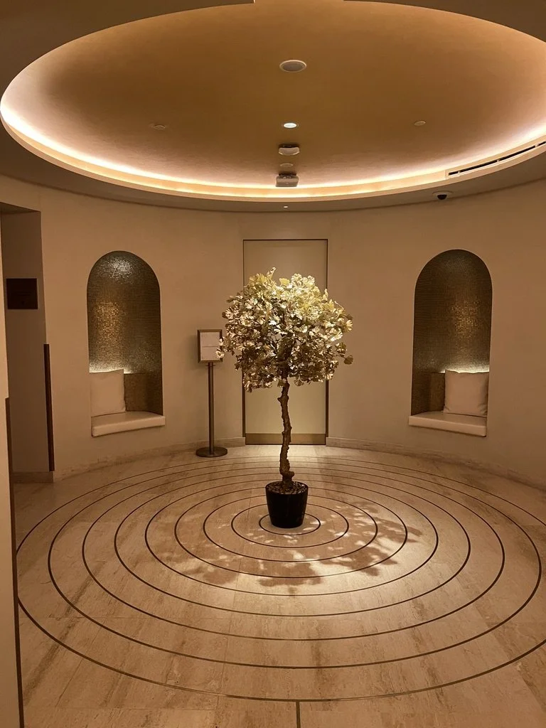 Golden entry to Cinq Mondes Spa at Raffles The Palm Dubai with a golden tree and two in-wall seating areas with cushions.