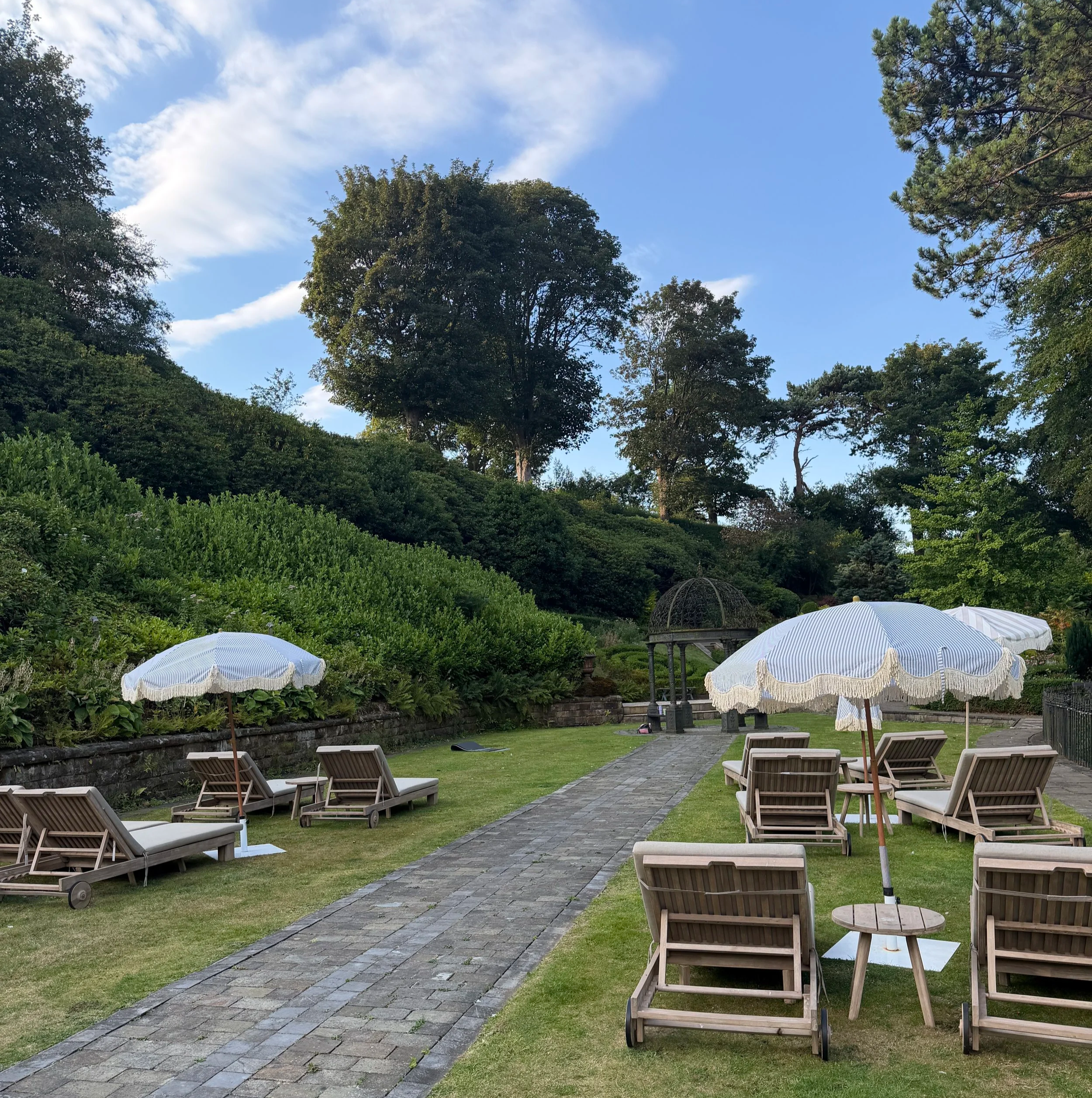 Cream and wooden loungers on the lawn with gardens in the background.