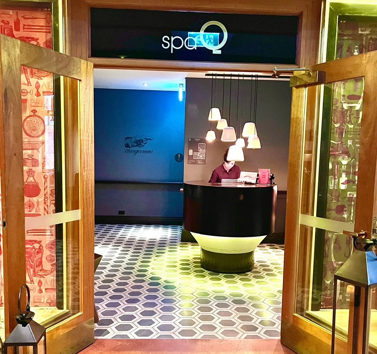 QT Sydney spa entry with golden door and black and white hexagon tiled floor leading to round welcome desk with hanging lights above.