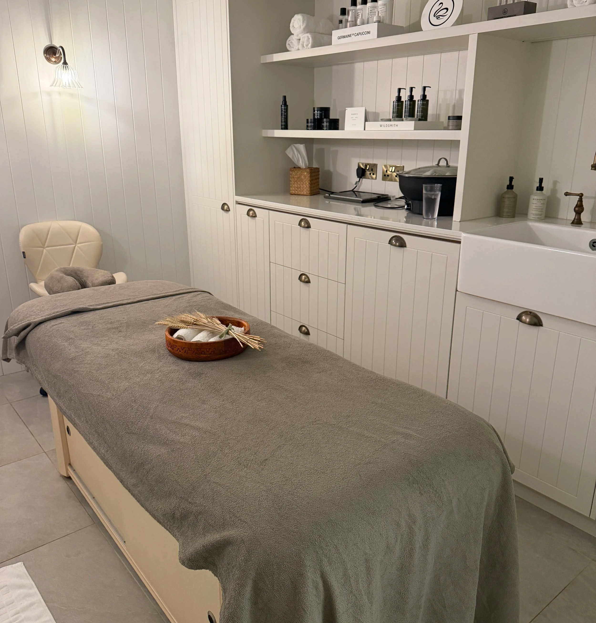 Treatment room with cream units behind with Wildsmith products on and a massage bed with a brown cover on.
