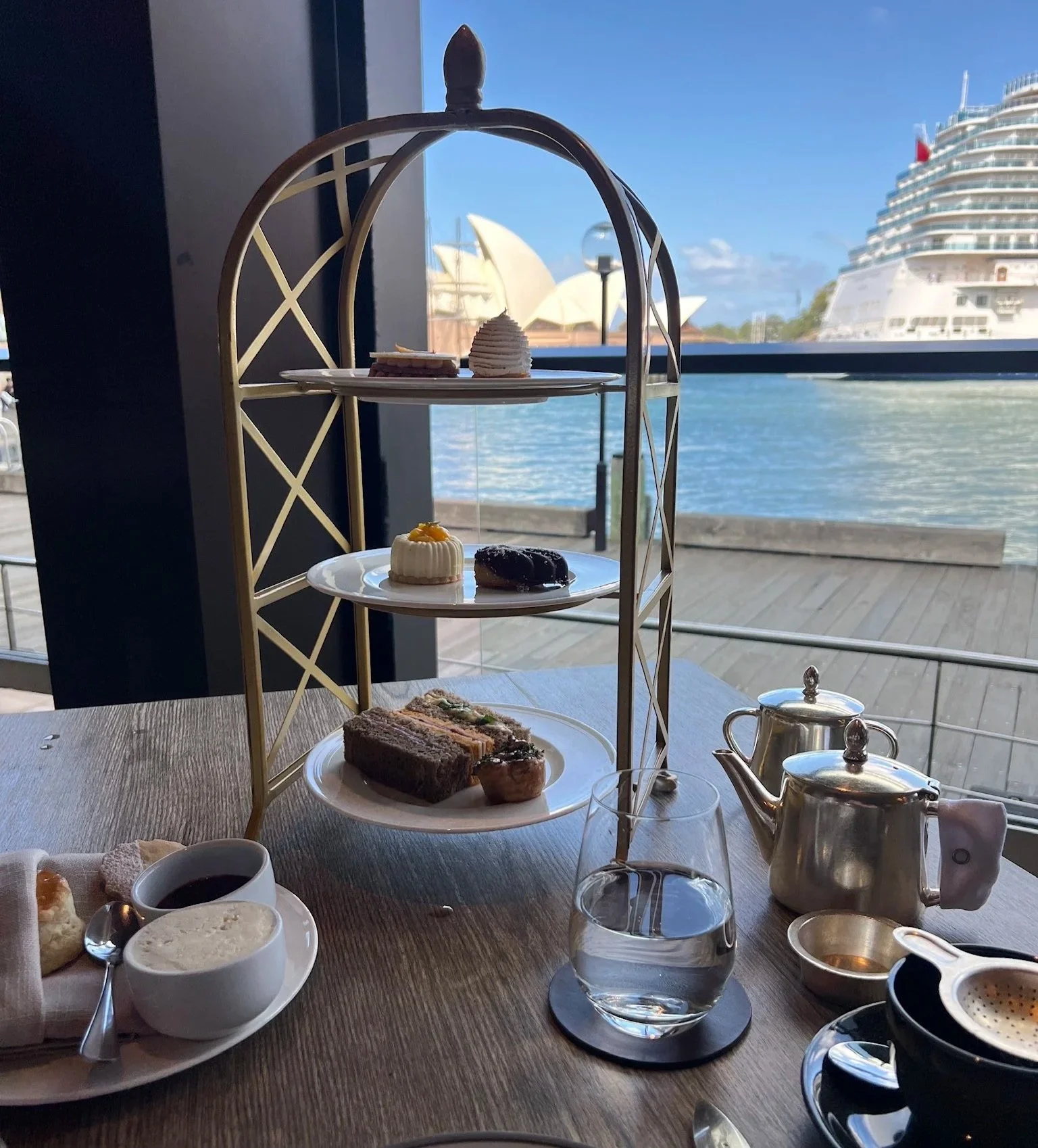 The Dining Room afternoon tea at  Park Hyatt Sydney on a three tiered platter with cruise ship and Sydney Opera House in the background.