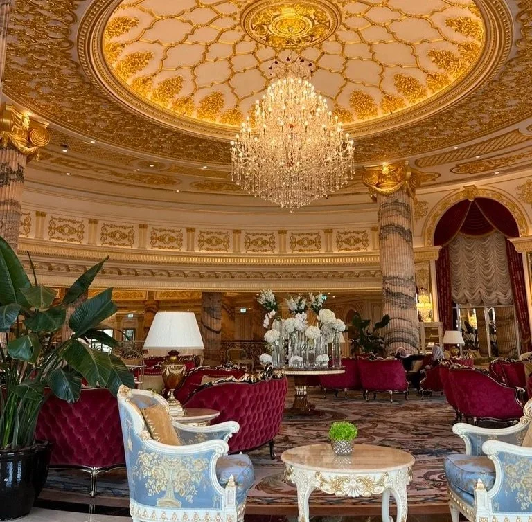 Raffles The Palm Blüthner Hall gilded ceiling with chandelier and plush red and blue gold seating.