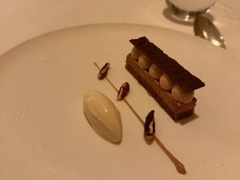 Chocolate mousse dessert on a white, round plate and banana ice cream on the left, three pecans on banana purée and the cake and mousse dissertation tot he right.