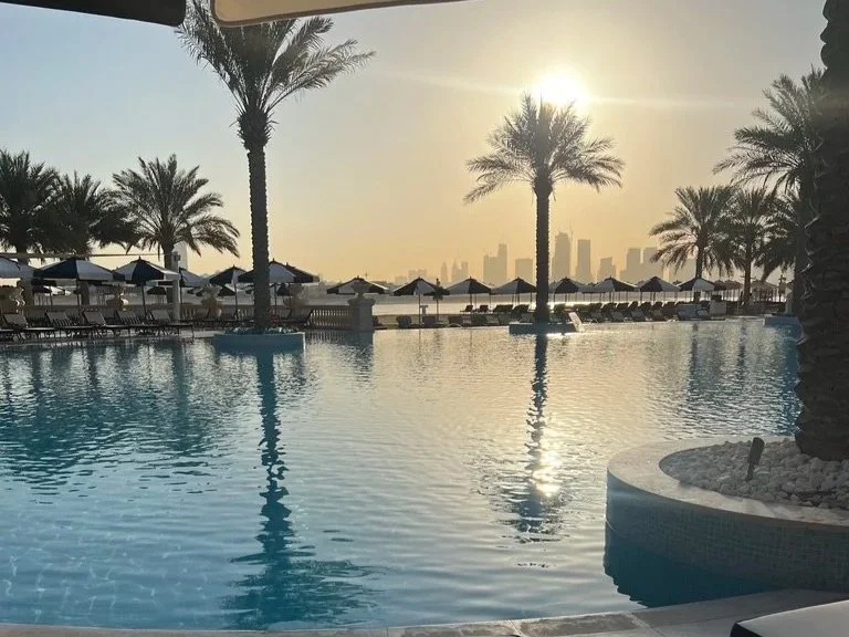 Raffles The Palm early morning first light by the outdoor pool with sun loungers and palm trees in the background.
