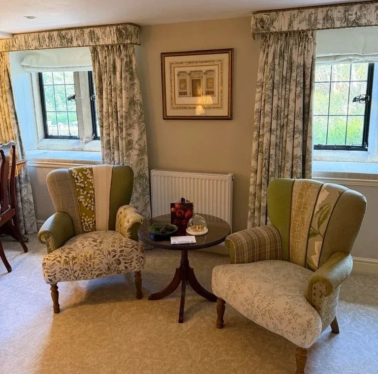 Cosy chairs with mixed upholstery with a round wooden table in-between with apple tarts, welcome card and dates on the table.