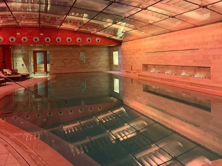Lucknam Park swimming pool at night with lights above and a lit fire on the right hand side and loungers on the left.