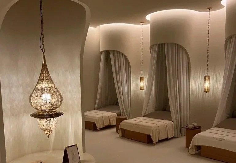 Raffles The Palm cream and golden spa relaxation area with three individual curtained pods with blankets and a Moroccan style light at the front.