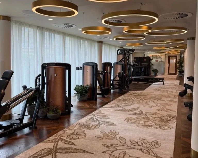 Gym at Grantley Hall with machine weight machines on the left and cardio equipment in the background and gold circle lights above.