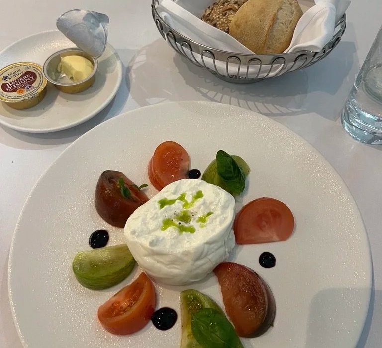 Tomato, basil, burrata salad with bread basket and butter in Emirates first-class lounge.