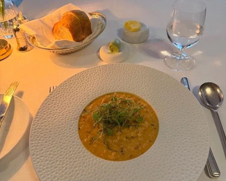White crab risotto with crispy leeks in Fletchers at Grantley Hall with a silver plater and two chunks of sourdough bread and two butters on marble rounds and a glass of water.