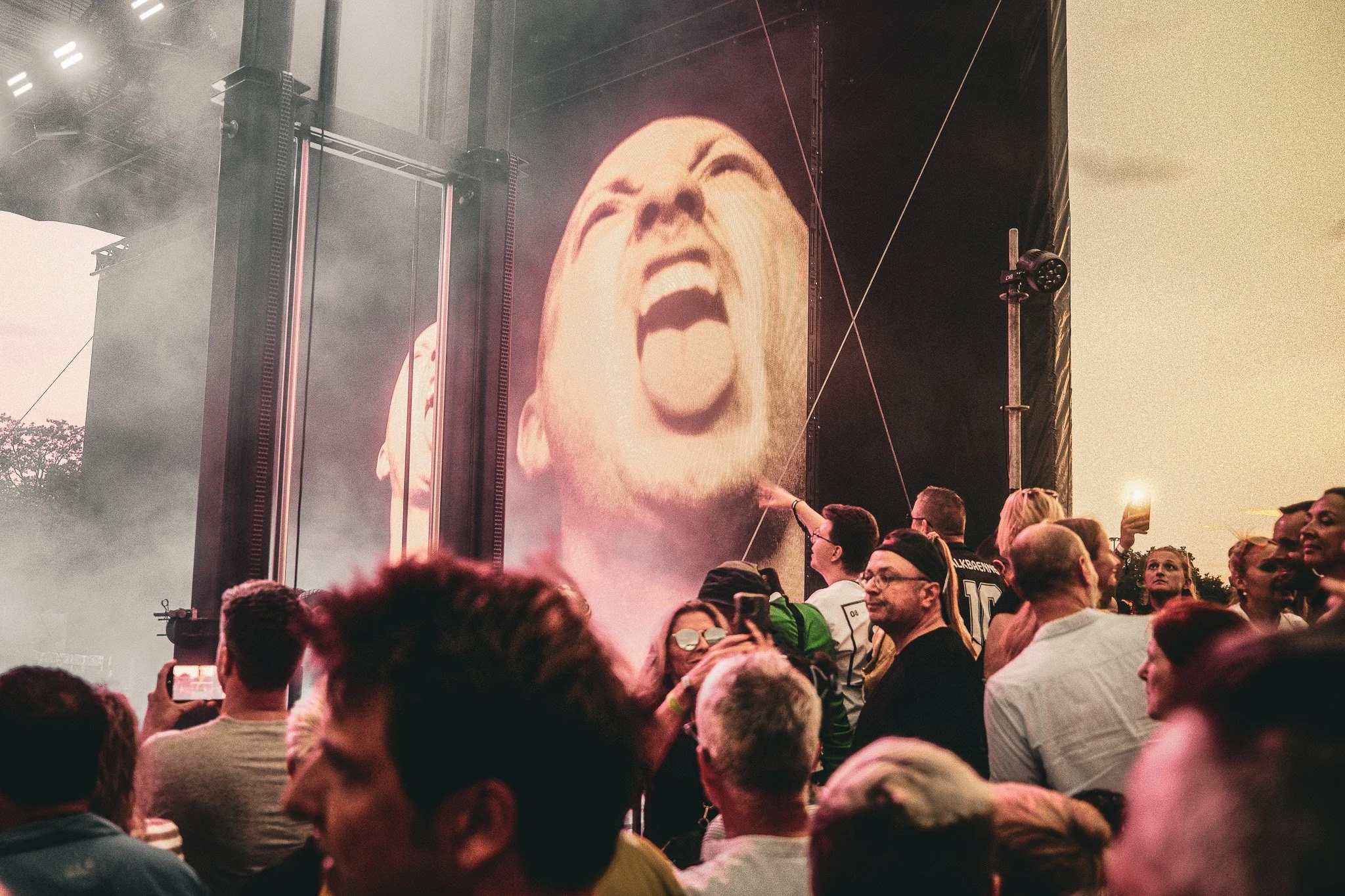 Menschenmenge bei einem Konzert mit einer großen Leinwand, die ein lachendes Gesicht zeigt.