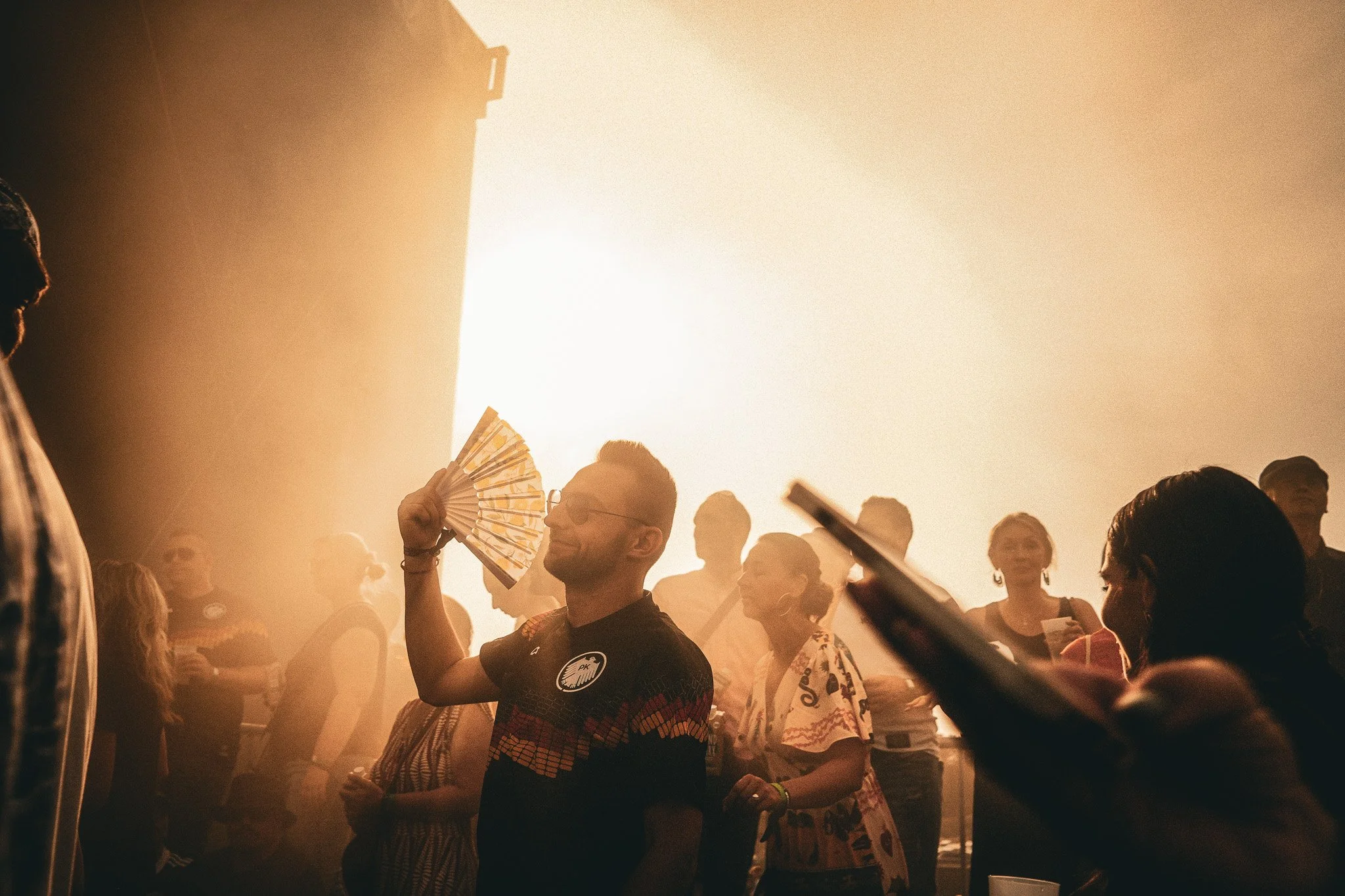 Menschenmenge bei einem Festival oder Konzert, einige tragen Sonnenbrillen und lassen sich von der warmen Sonnenstrahlung beleuchten.