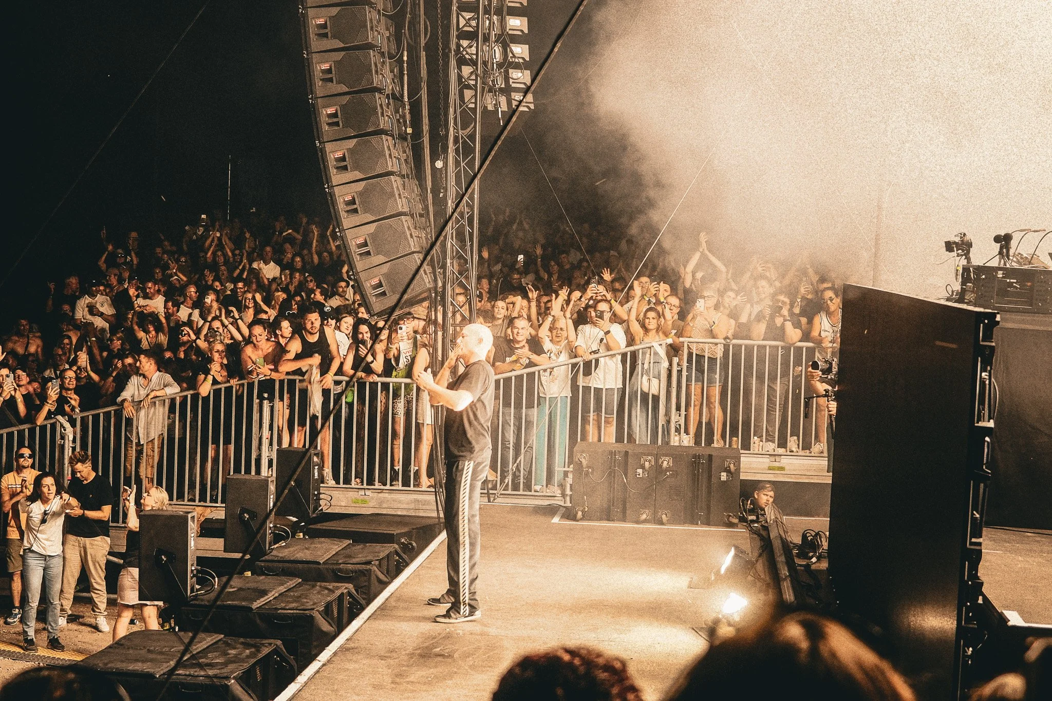 Menschen auf einer Konzertbühne und im Publikum, das Konzert feiert mit Begeisterung, Bühnenausrüstung und Scheinwerfer sind sichtbar.