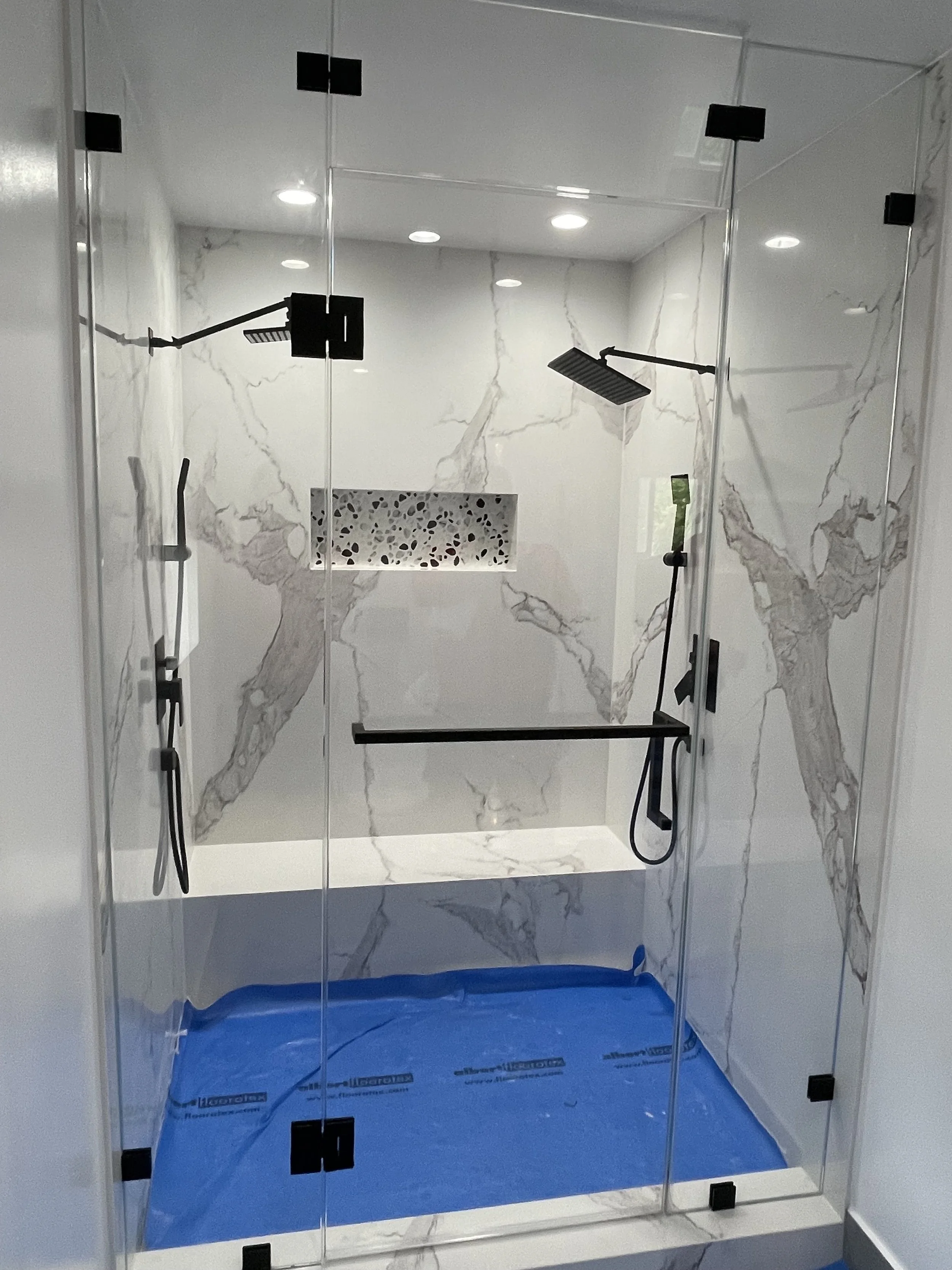 A modern walk-in shower with marble walls, and black fixtures.