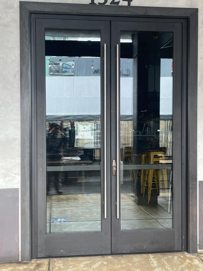 Double glass doors with metal handles leading into a building, reflecting the street scene outside.