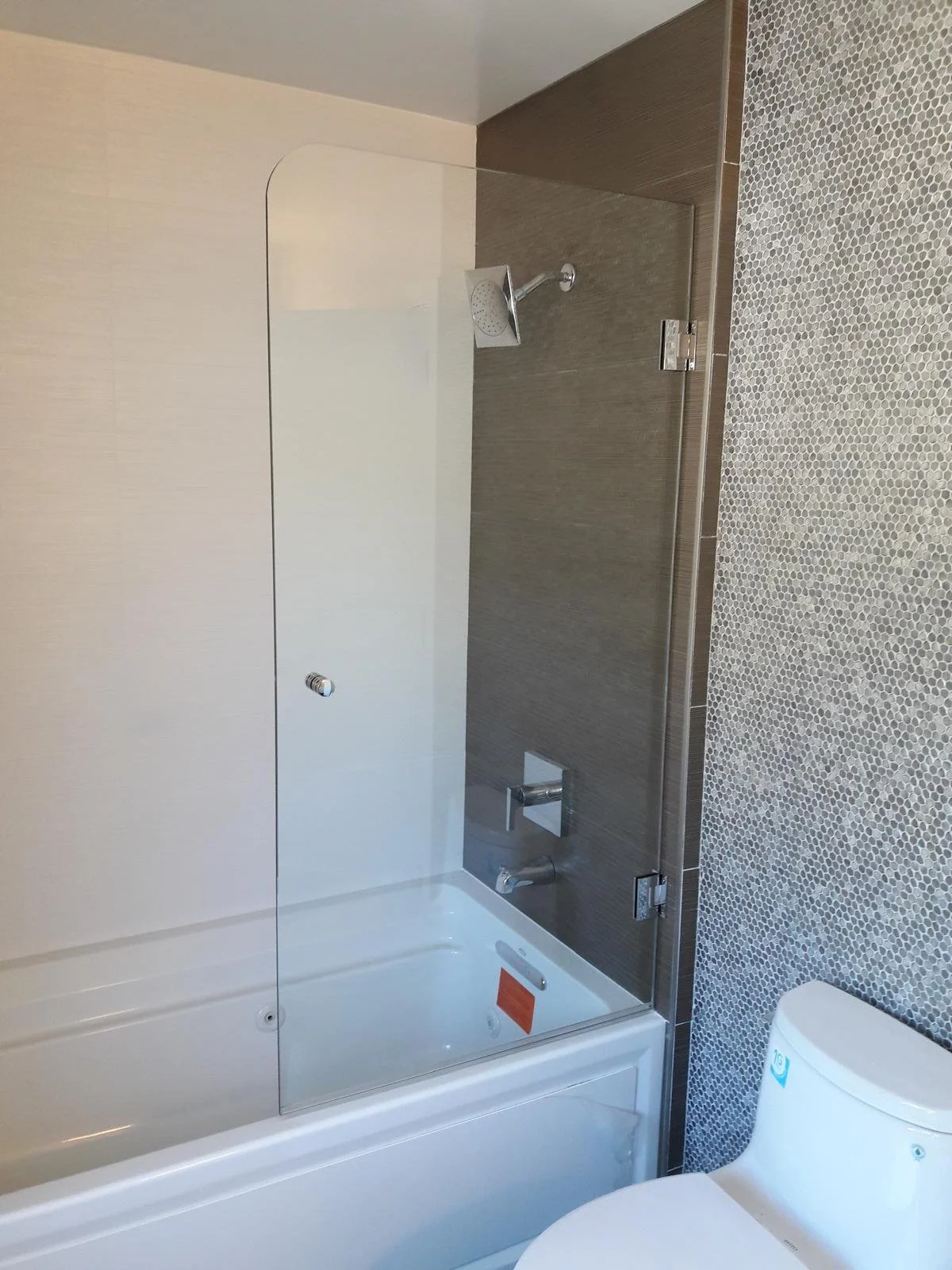 Modern bathroom with shower and glass panel, dark brown tiled wall, and pebble stone floor.
