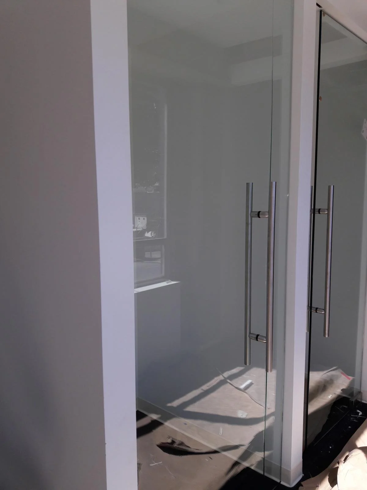 Glass double doors with metal handles leading into a room, seen through a glass wall reflecting the room's interior.