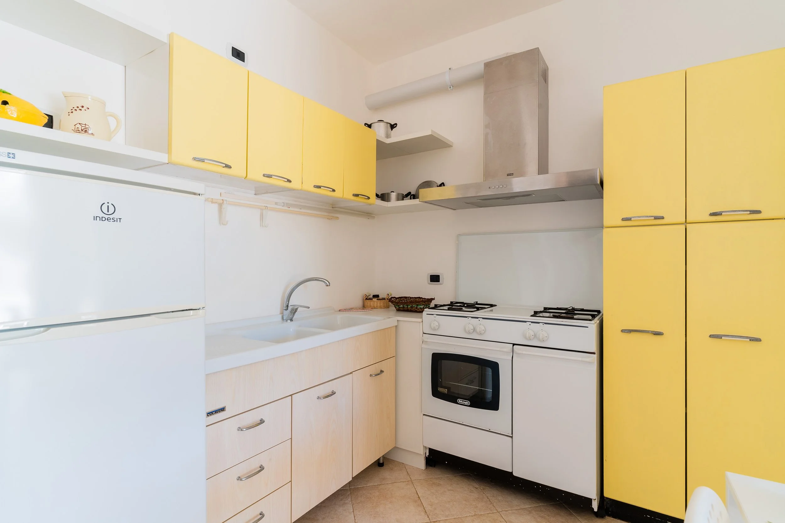 A kitchen with yellow cabinets, a white stove, and a white refrigerator. There is a sink with a silver faucet and a few kitchen items on the countertops and shelves.