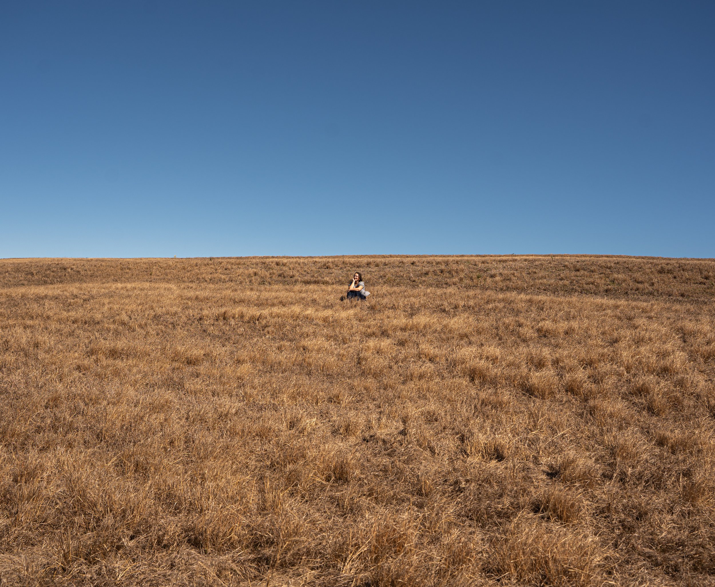 A person sitting on dry grass under a clear blue sky.